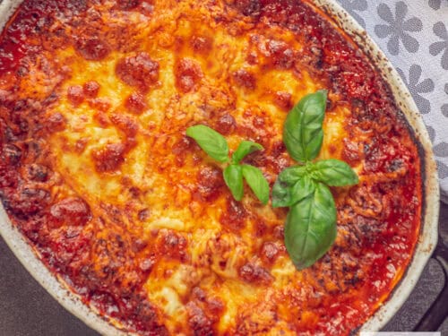 Een vierkante foto van een deel van een ovenschaal gevuld met lasagne met bolognesesaus en gesmolten kaas