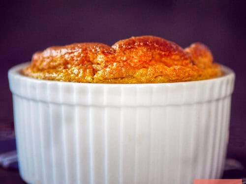 Een vierkante foto van een ramekin waar een aardpeer souffle naar boven is gerezen.