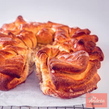 Een vierkante foto met een deel van een kaneelsuiker twist brood op een wit bakpapier.