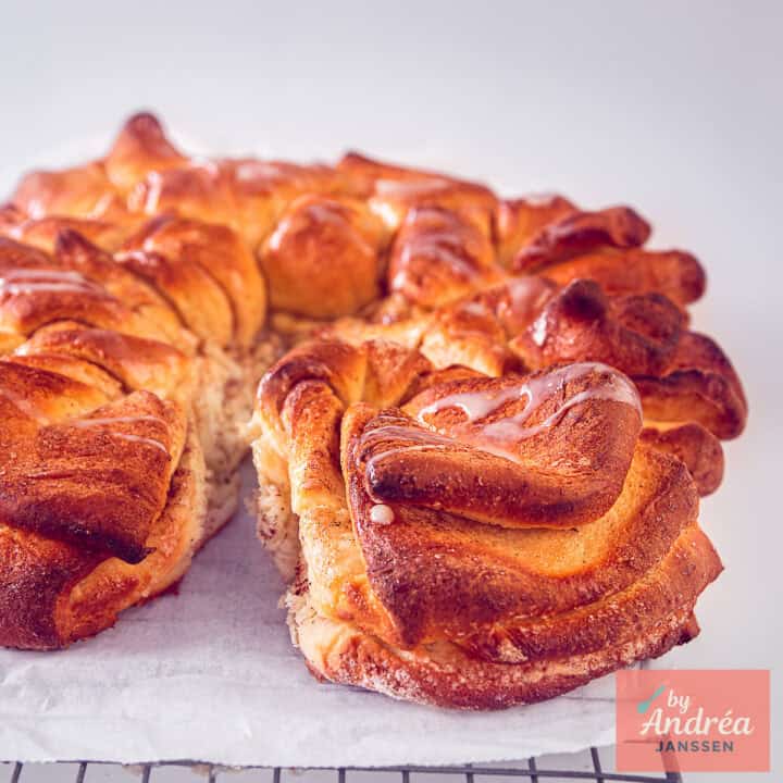 Een vierkante foto met een deel van een kaneelsuiker twist brood op een wit bakpapier.