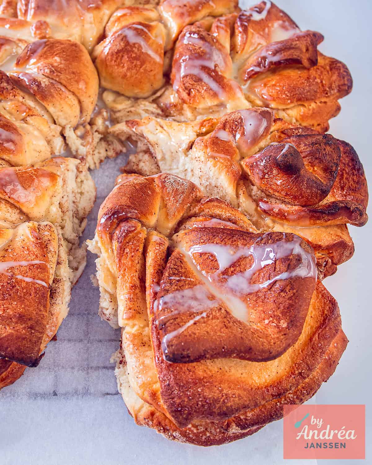 Een foto van bovenaf van een kaneelbrood op een bakpapier met een gecondenseerde melk swirl.