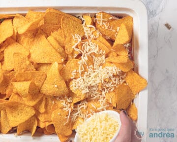 Geraspte kaas wordt op de nacho's in een witte ovenschaal gestrooid.