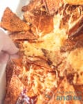 een deel van een Mexicaanse nacho ovenschotel. Een hand pakt een nacho chips met gesmolten kaas uit de ovenschaal
