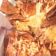 een deel van een Mexicaanse nacho ovenschotel. Een hand pakt een nacho chips met gesmolten kaas uit de ovenschaal
