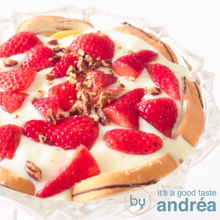 Een vierkante foto met een glazen schaal gevuld met laagjes cake, room, aardbeien en pecannoten