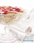 Aardbeien trifle in een glazen schaal met voet. Op een witte achtergrond. Aan de rechterzijde een servet en lepel.
