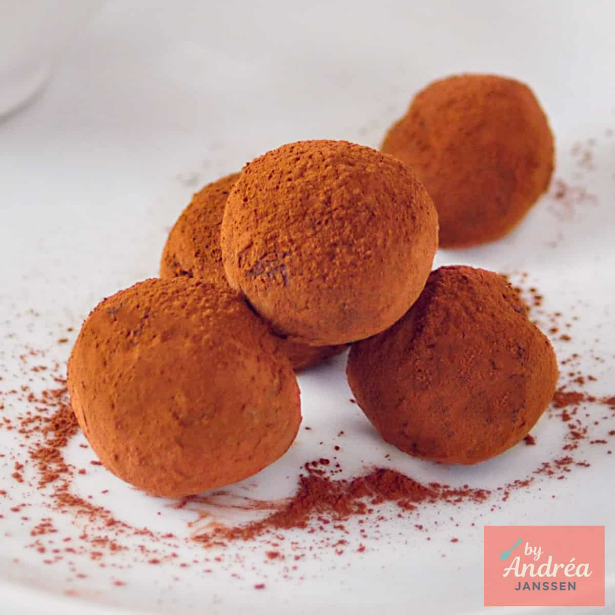 Een vierkante foto met vijf sinaasappel en chocolade truffels ope en witte ondergrond.