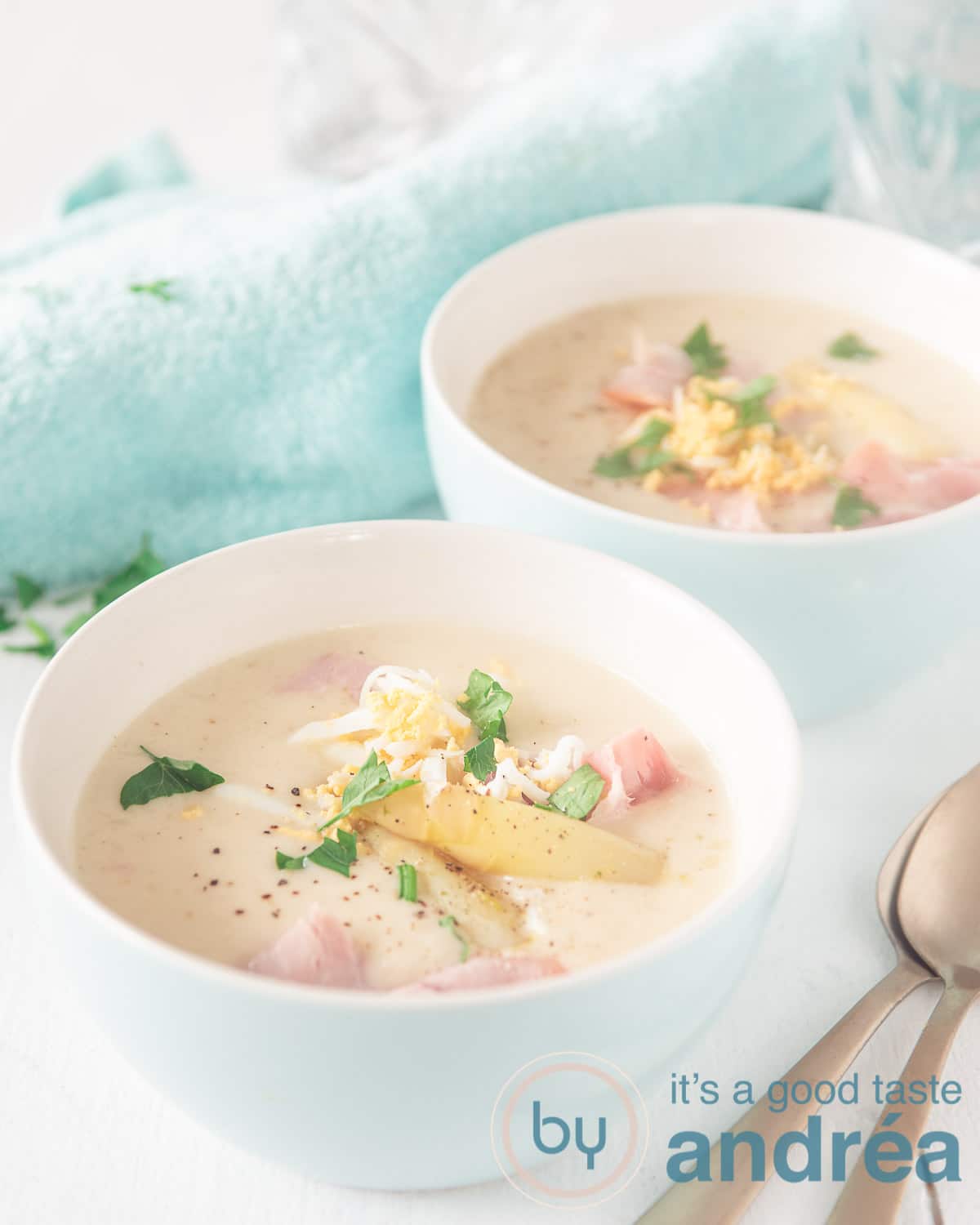 Two white bowls filled with a creamy asparagus soup and topped with ham and grated egg