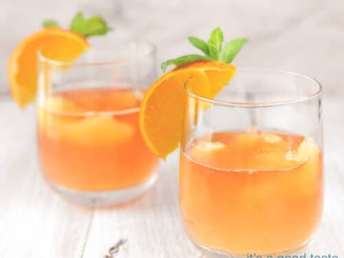 Op een witte ondergrond staan twee glazen met sinaasappel oranje cocktail