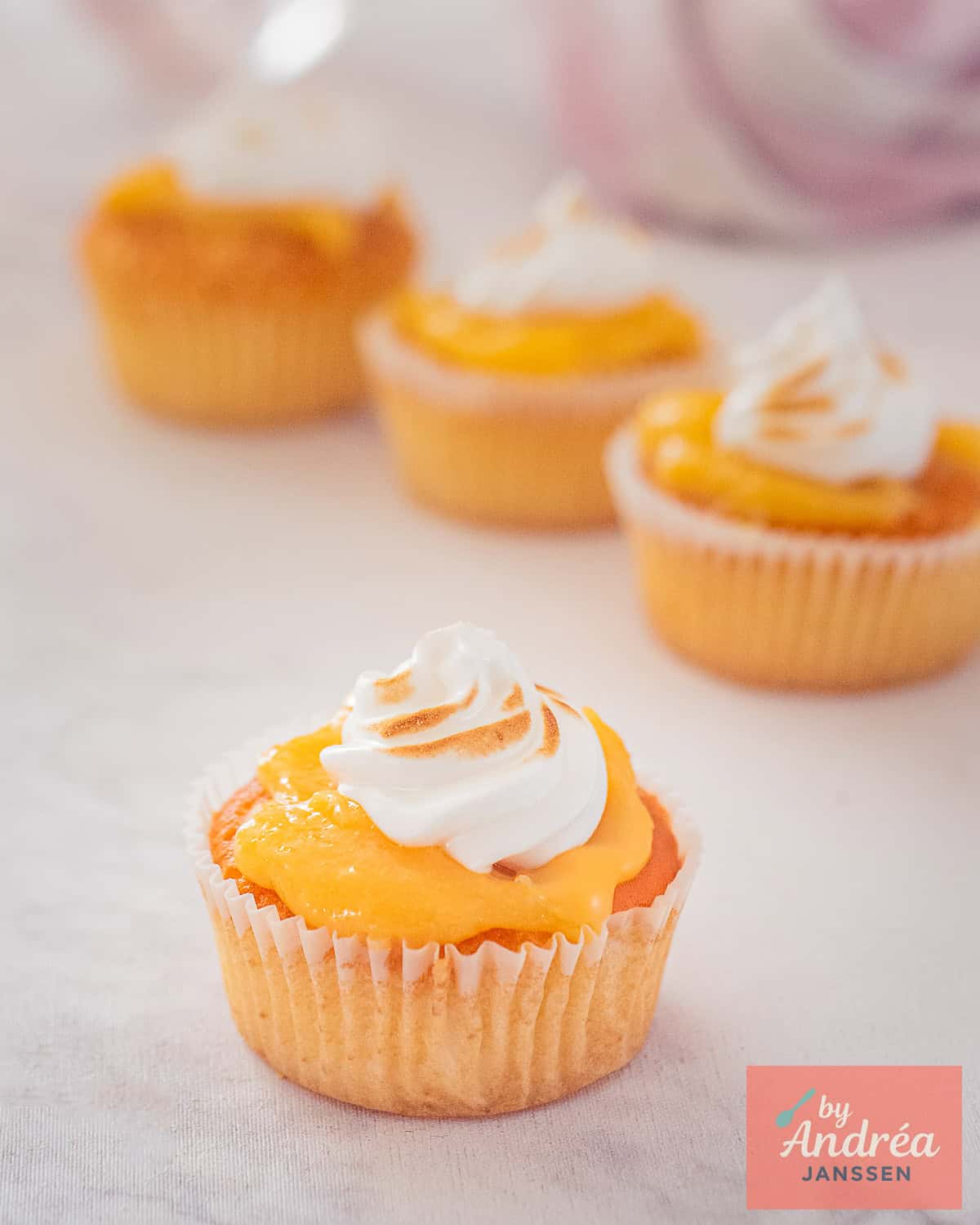 Vier lemon merengue cupcakes op een wit marmeren ondergrond met lemon curd en meringue