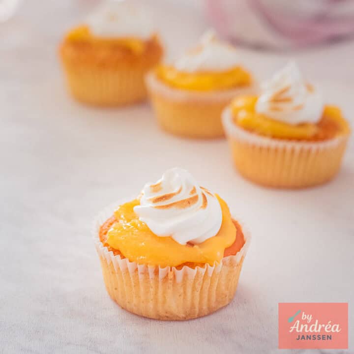 Vier citroen cupcakes met lemon curd en meringue op een wit marmeren ondergrond.