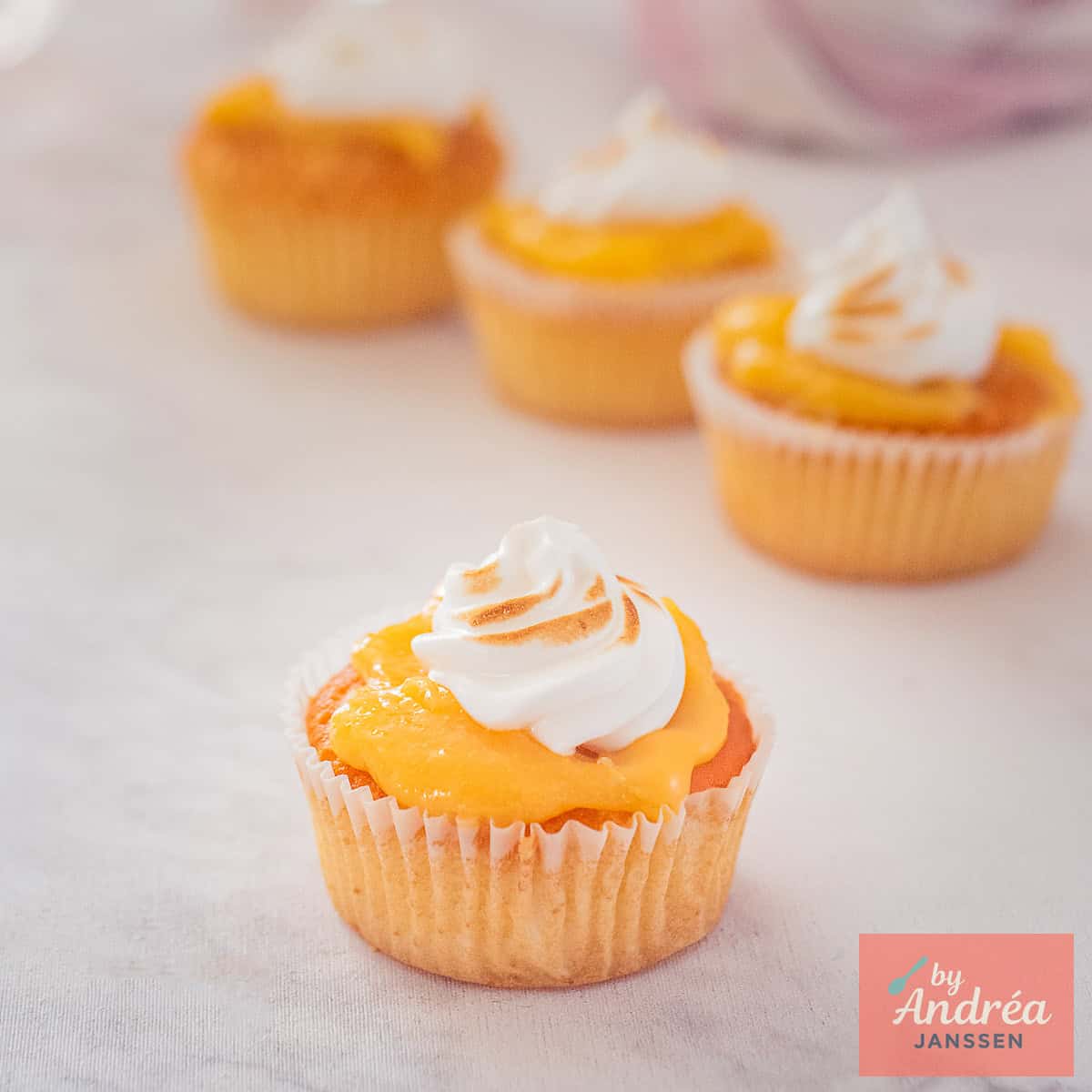 Vier citroen cupcakes met lemon curd en meringue op een wit marmeren ondergrond.