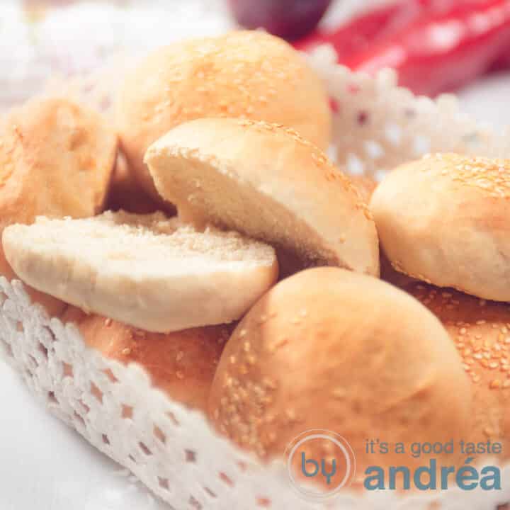 Een vierkante foto van een witte schaal gevuld met hamburgerbroodjes. Eén van de broodjes is opengesneden