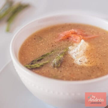 Een vierkante foto met een witte kom met Mosterdsoep met groene asperges en zalm