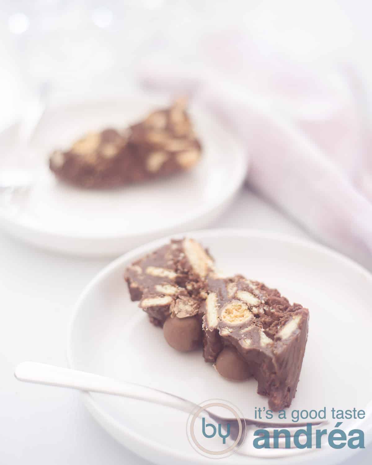 Een hoogte foto met twee witte bordjes met een plak arretjescake met Maltesers. Twee vorken liggen op het bord erbij. In de bovenhoek een roze witte theedoek