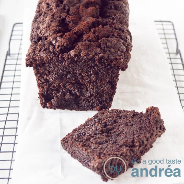 A Chocolate zucchini pound cake, one slice cut of laying in front on a baking paper on a rack.