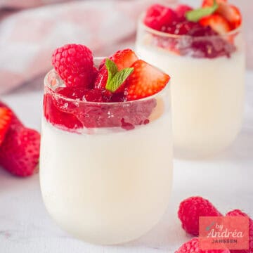 Een vierkante foto met twee glaasjes achter elkaar met yoghurt ijs, aardbeienjam en rood fruit.