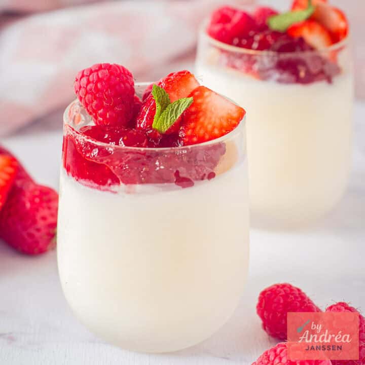 Een vierkante foto met twee glaasjes achter elkaar met yoghurt ijs, aardbeienjam en rood fruit.