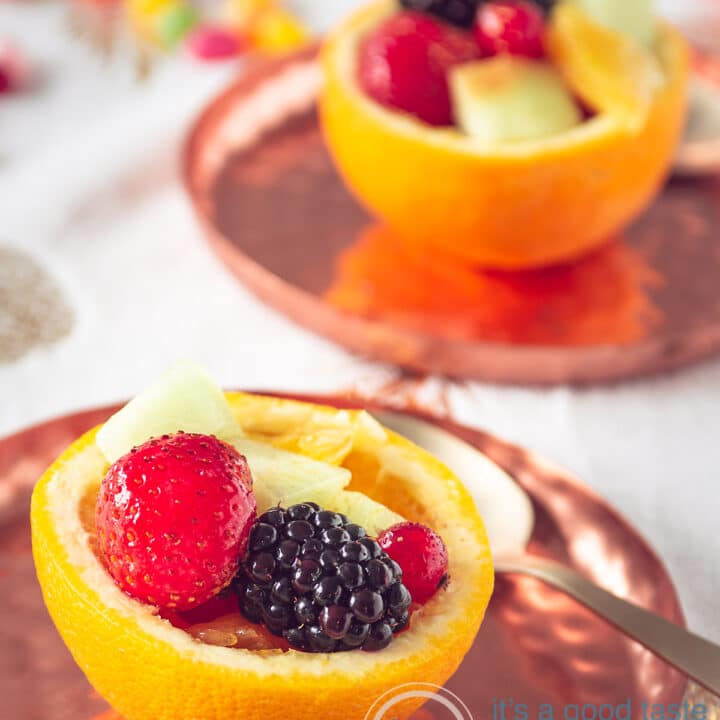 Twee uitgeholde sinaasappels gevuld met fruit op een koperen bord