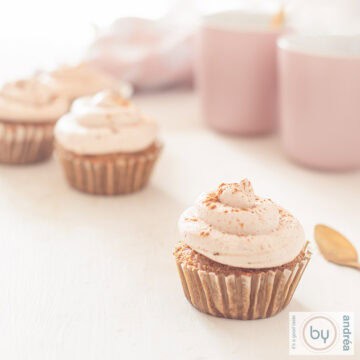 Een vierkante foto met een aantal cupcakes met tiramisu op een witte ondergrond. Aan de rechterzijde twee roze kopjes.