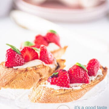 twee bruschette met roomkaas, daarop aardbeien en creme balsamico. Op de achtergrond servies