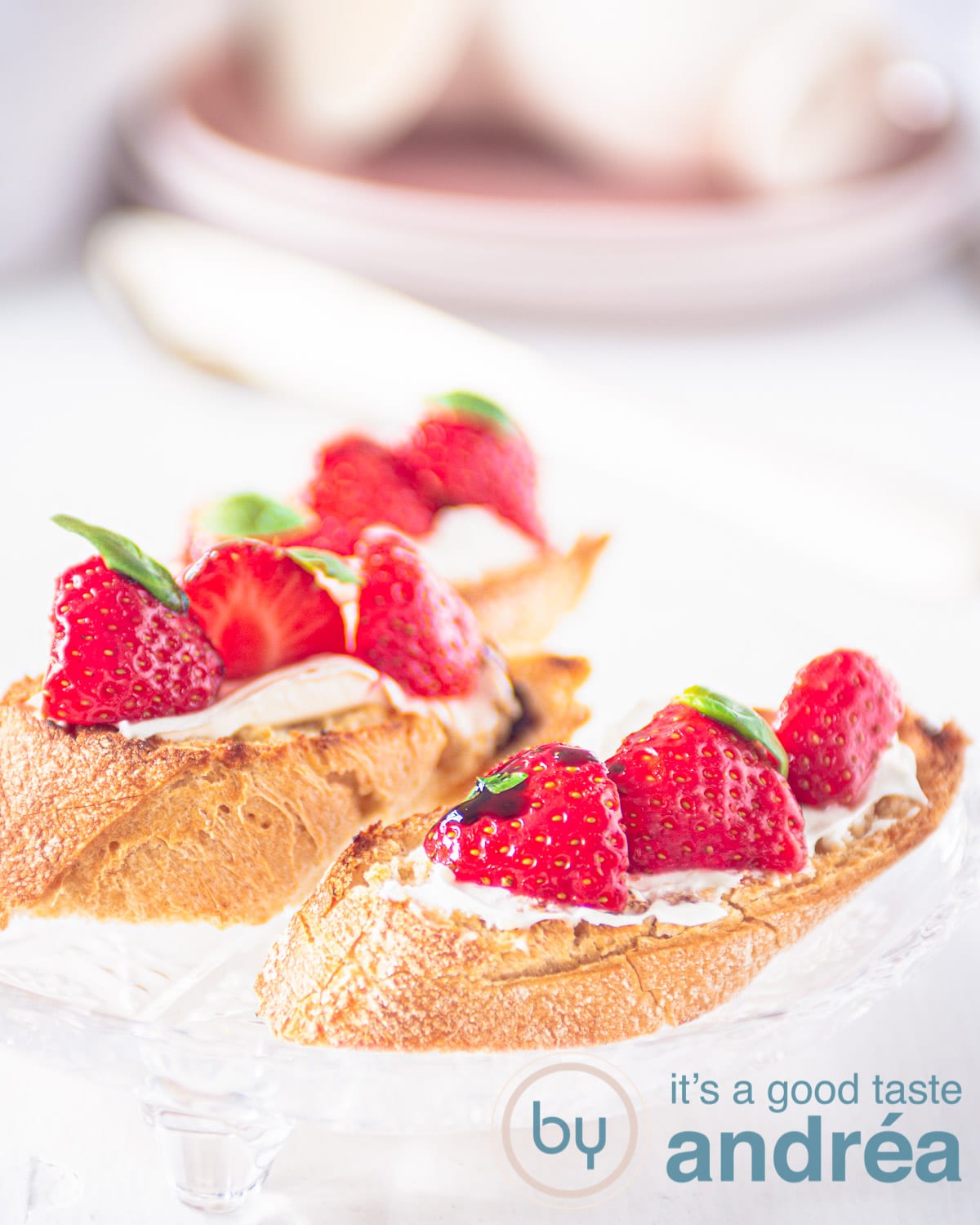 twee bruschette met roomkaas, daarop aardbeien en creme balsamico. Op de achtergrond servies