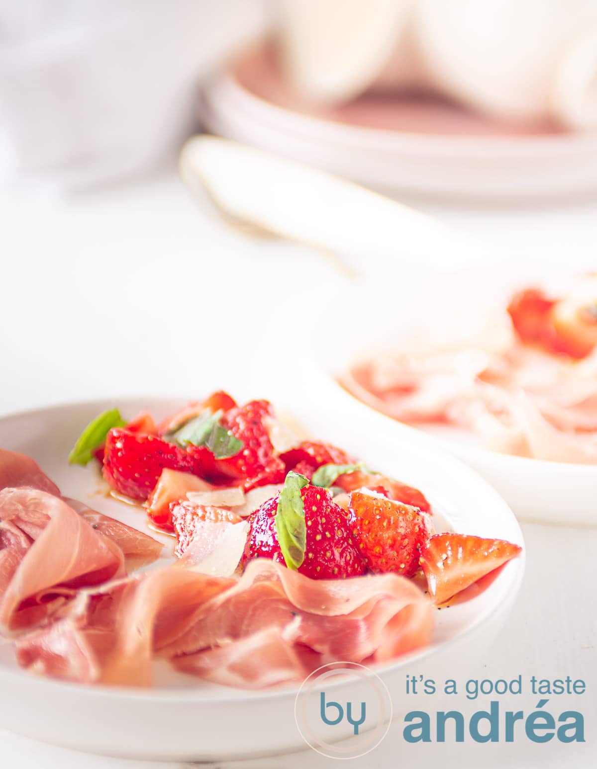 Op een wit bord aardbeien gemarineerd in creme balsamico met ham, op de achtergrond servies