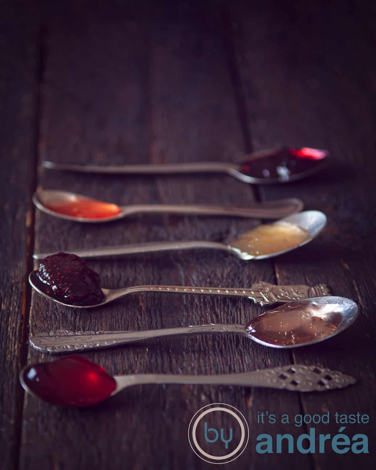 Een donkere achtergrond met 6 lepels gevuld met verschillende soorten jam