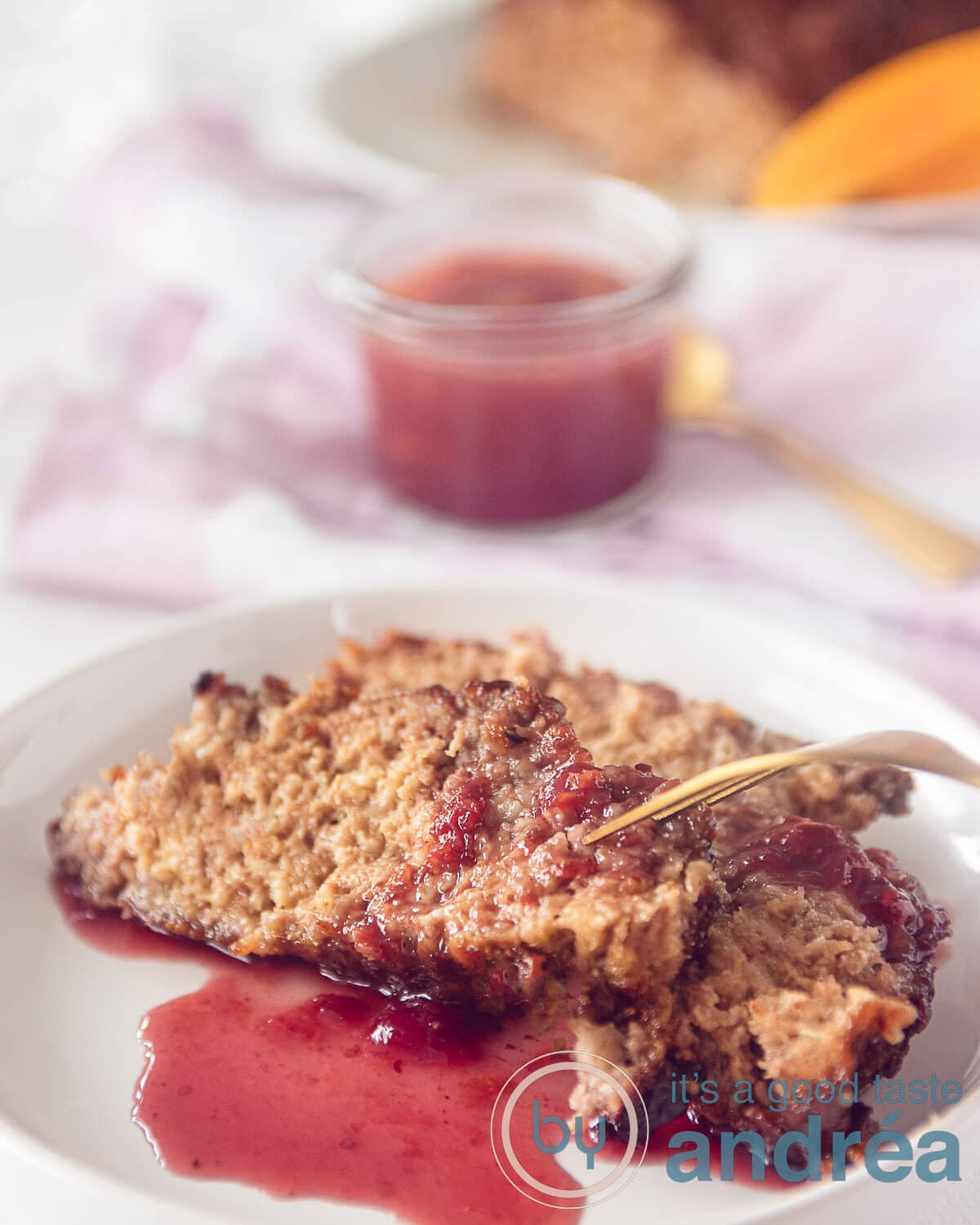 Een bord met daarop twee plakken gehaktbrood en wat port saus. In de achtergrond meer saus en gehaktbrood