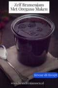 Een pot met bramenjam met oregano op een jute lap op een donkere ondergrond. Een tekst: Zelf Bramenjam met Oregano Maken