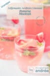 Twee glazen gevuld met aardbeien mocktail op een witte ondergrond met een gevulde sapkan erachter. Een tekstoverlay staat erboven.