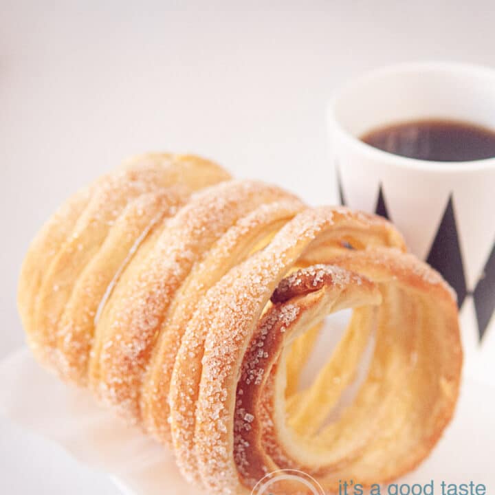 Een schoorsteen cake (koekje) op een witte achtergrond met een kopje koffie in een wit met zwarte ruitjes mok