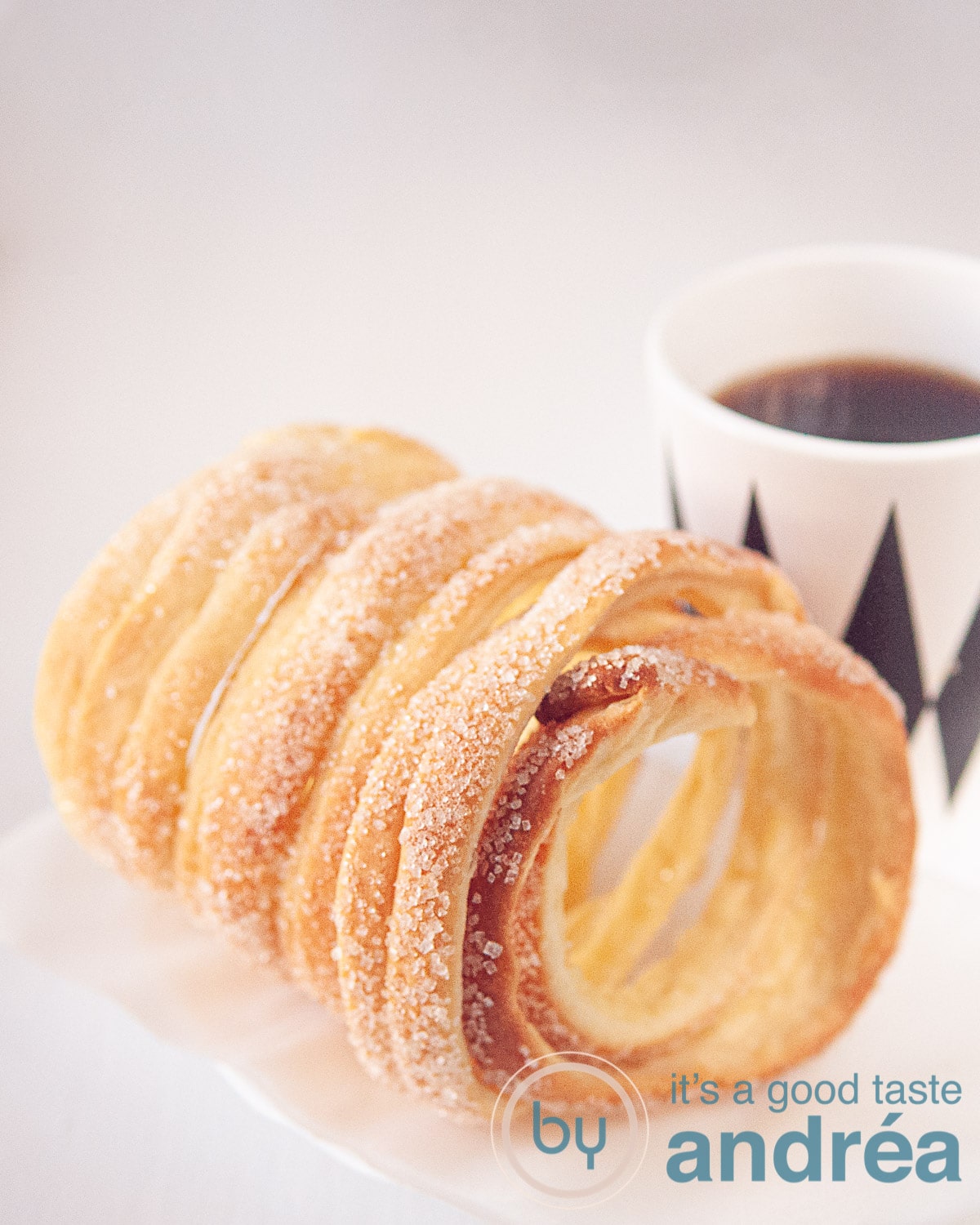 Een schoorsteen cake (koekje) op een witte achtergrond met een kopje koffie in een wit met zwarte ruitjes mok