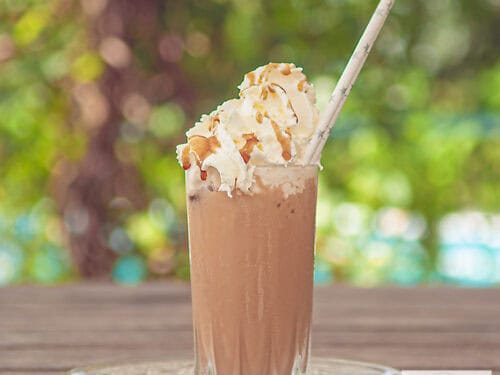 Een vierkante foto van een frappuccino op een houten tafel.
