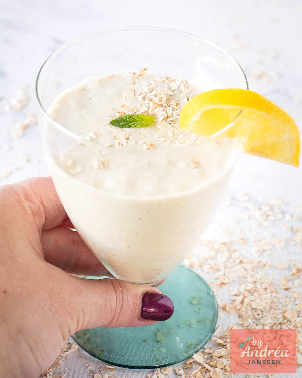 Een hand pakt een glas met een frisse banaan smoothie met citroen, munt en kokosmelk
