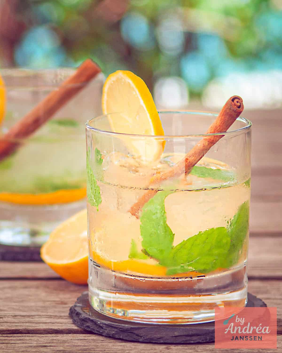 Een frisse cocktail met caipirinha, gemberthee, munt en citroen, schuin achtere elkaar op een houten ondergrond.