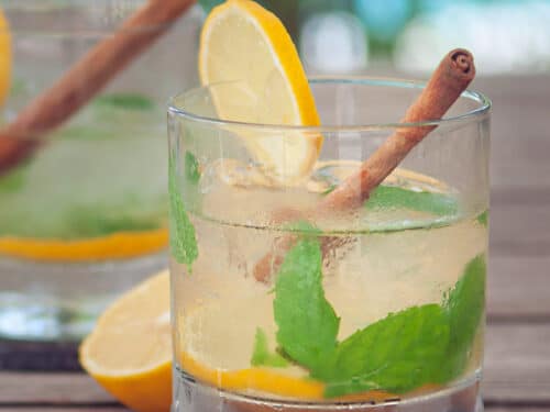 Twee glazen Caipirinha thee cocktail met munt, kaneel en citroen tegen een zomerse achtergrond