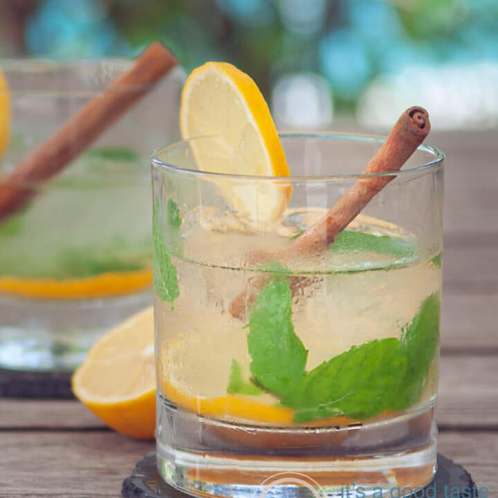 Twee glazen Caipirinha thee cocktail met munt, kaneel en citroen tegen een zomerse achtergrond