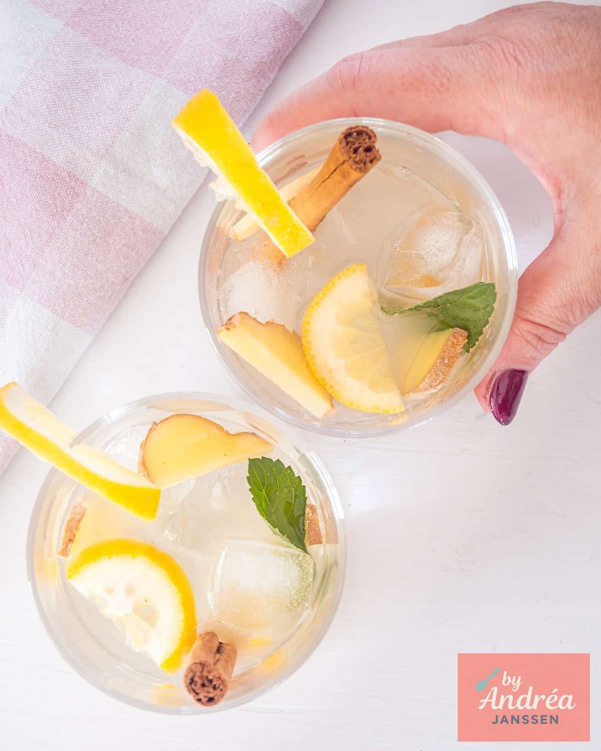Een foto van bovenaf van twee glazen met gember caipirinha met munt en citroen. Een glas wordt vastgepakt.