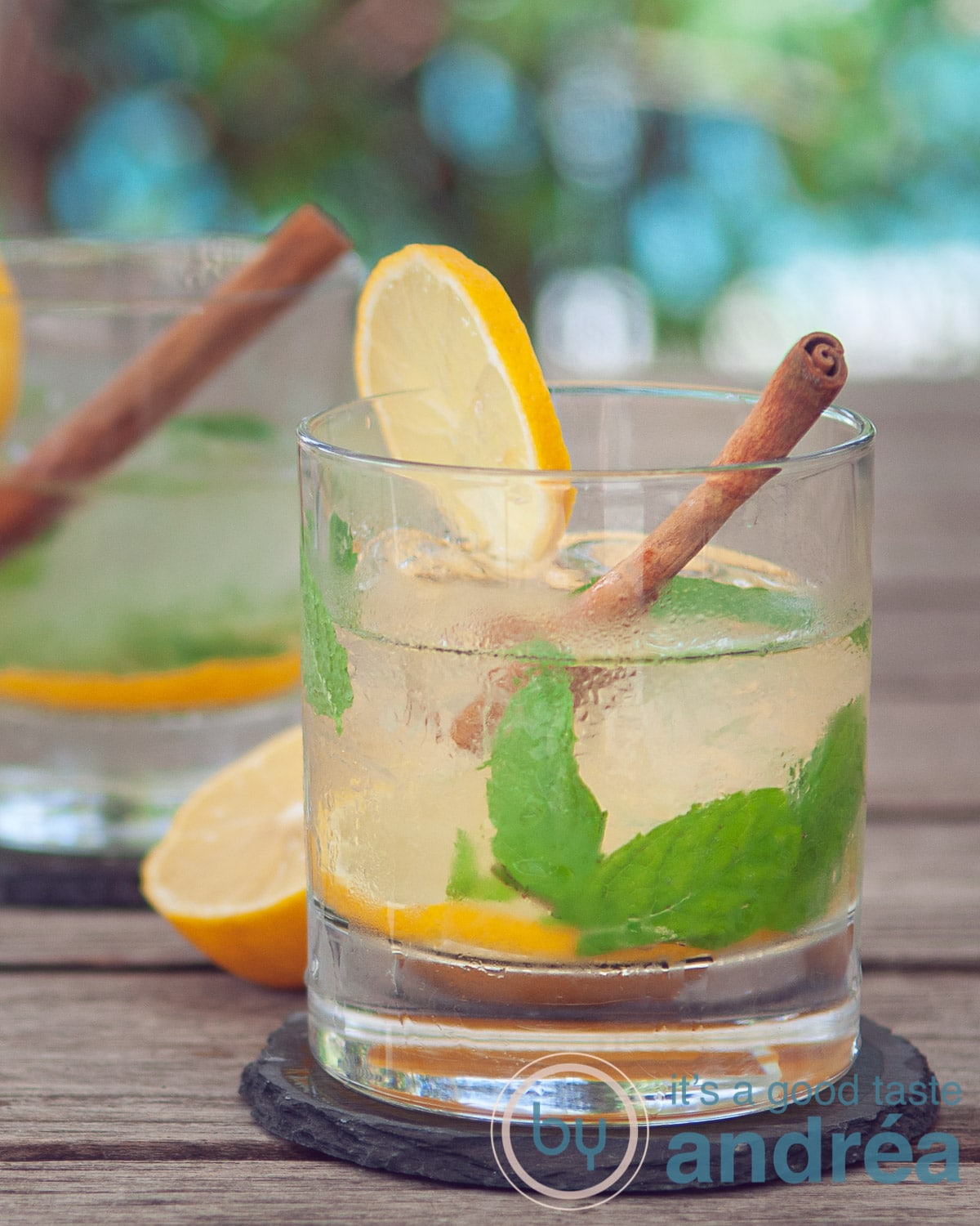 Twee glazen Caipirinha thee cocktail met munt, kaneel en citroen tegen een zomerse achtergrond