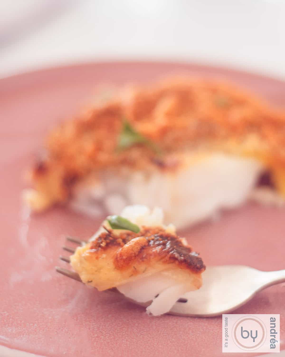 Een foto van kabeljauw met een laagje kaas. Een vork prikt een stukje vis.