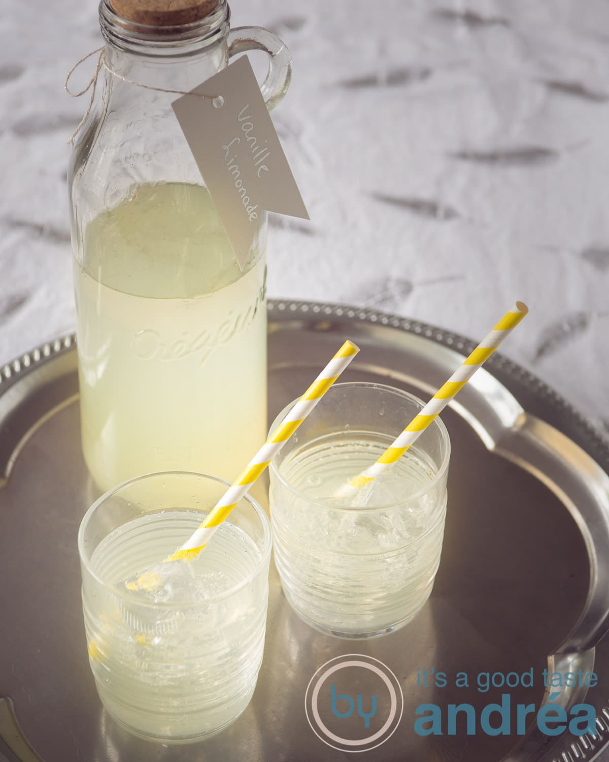 een fles vanille limonade met twee gevulde glazen met geel witte rietjes