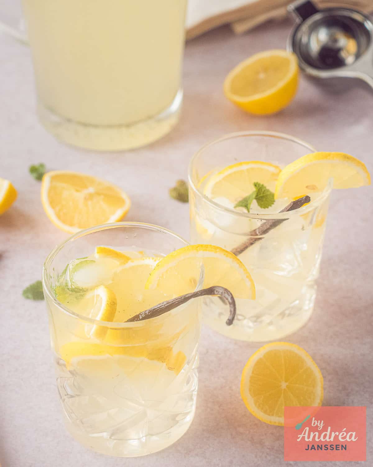 Twee glazen met Vanille limonade met citroen en een karaf in de achtergrond.