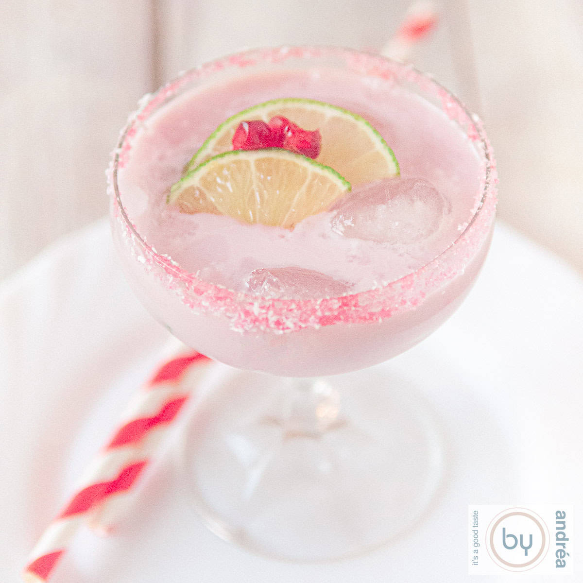 Een vierkante foto van een champagne glas gevuld met een margarita cocktail met limoen en granaatappel. Een witte ondergrond