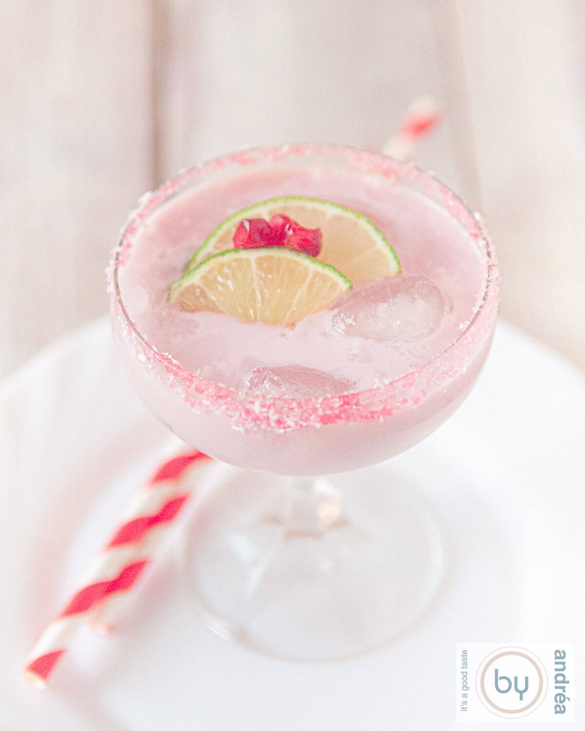 Een hoogtefoto met een champagne coupe gevuld met een kokos granaatappel margarita cocktail, gegarneerd met schijfjes limoen en granaatappelpitjes