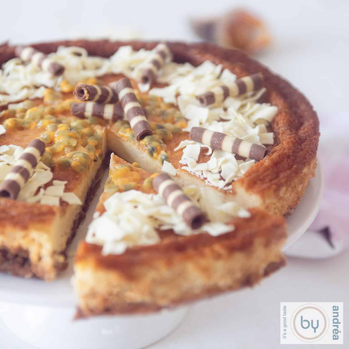 Een vierkante foto van een cheesecake met witte chocola en passievruchten. Een topping van vlokken en slagroom.