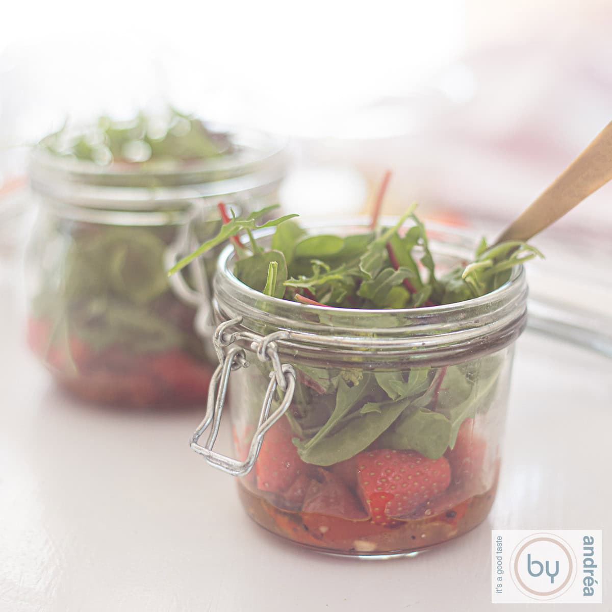 Een vierkant plaatje met twee potjes gevuld met frisse salade met sla, aardbeien en honing-mosterddressing