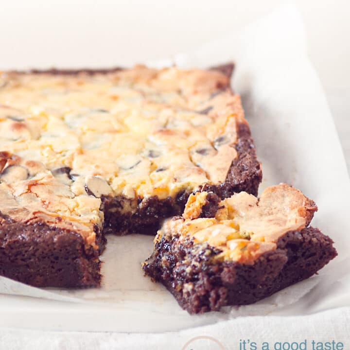 Een brownie met cheesecake waar een hoekje uit is gesneden op wit bakpapier