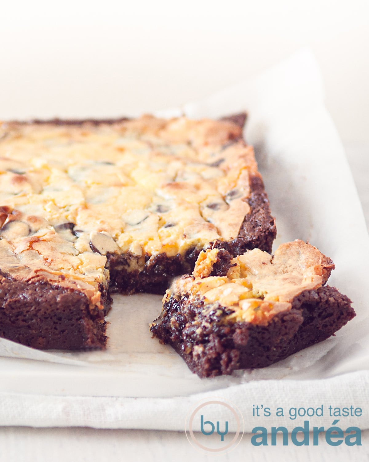 Een brownie met cheesecake waar een hoekje uit is gesneden op wit bakpapier