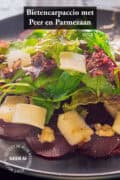 Een deel van een bord met carpaccio van bieten, Parmezaanse kaas, peer, walnoten en gemengde sla. Een tekst bovenin: bietencarpaccio met peer en parmezaan